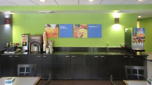 A breakfast bar with a green wall, a waffle maker, and a juice dispenser. - Comfort Inn & Suites Lantana - West Palm Beach South (Lantana)