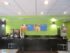 A breakfast bar with a green wall, a waffle maker, and a juice dispenser. - Comfort Inn & Suites Lantana - West Palm Beach South (Lantana)