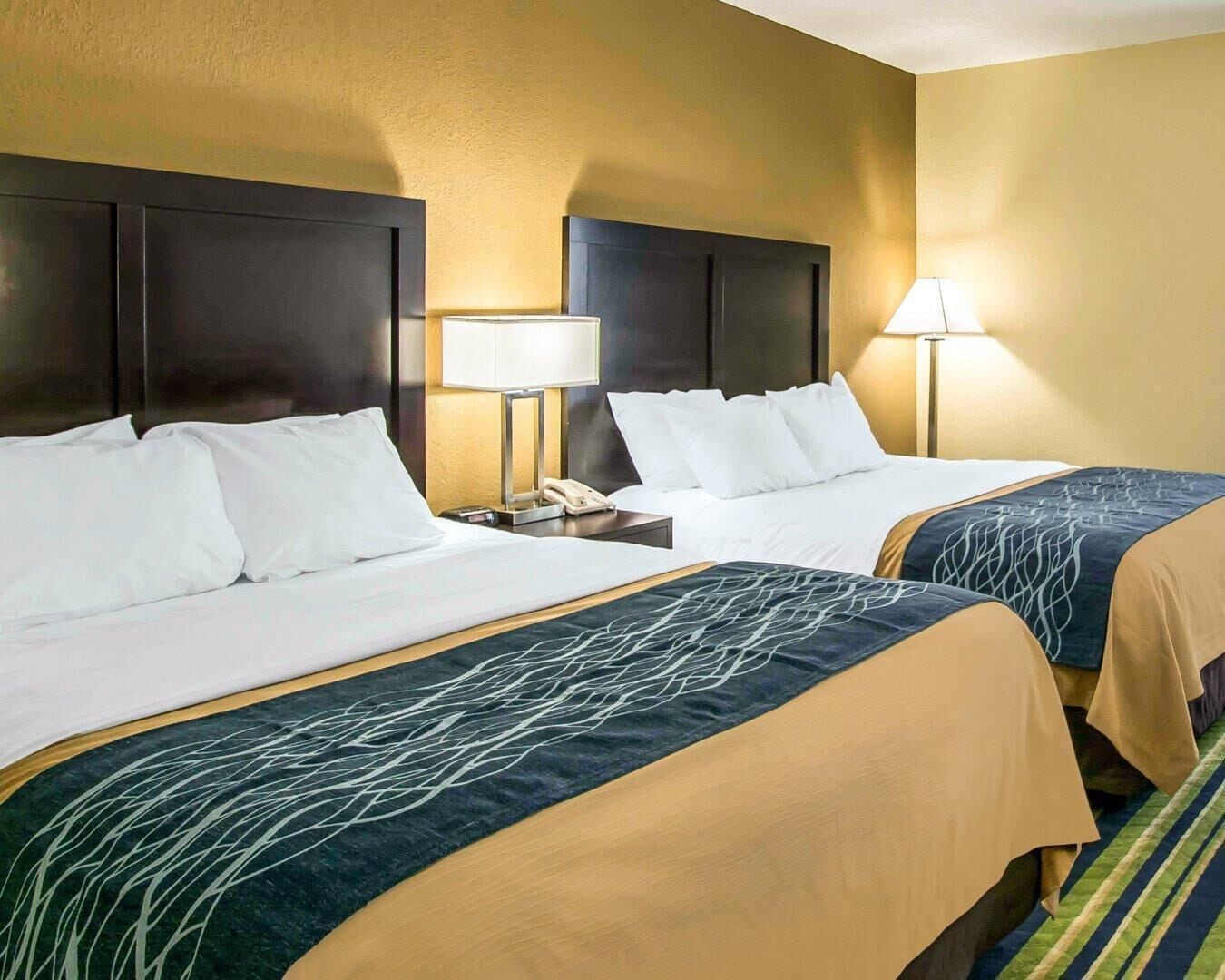 A hotel room with two beds, each with a headboard, bedside tables, lamps, and a telephone.
