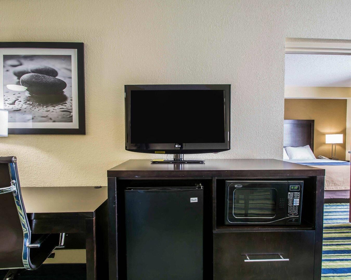 A hotel room with a flat-screen TV on a stand, a mini-fridge, and a microwave.