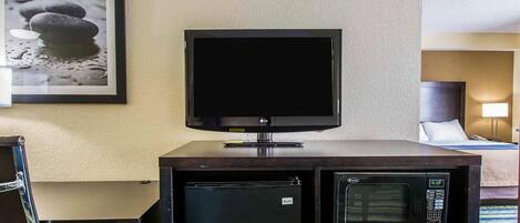 A hotel room with a flat-screen TV on a stand, a mini-fridge, and a microwave.