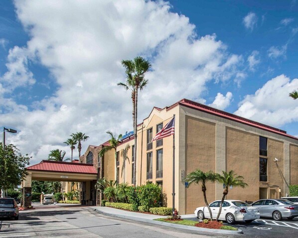 A hotel with a red roof, American flag, and palm trees. - Comfort Inn & Suites Lantana - West Palm Beach South (Lantana)
