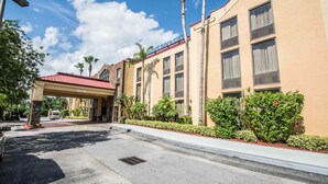A hotel entrance with a red roof, palm trees, and a clear sky. - Comfort Inn & Suites Lantana - West Palm Beach South (Lantana)