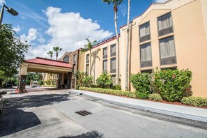 A hotel entrance with a red roof, palm trees, and a clear sky. - Comfort Inn & Suites Lantana - West Palm Beach South (Lantana)
