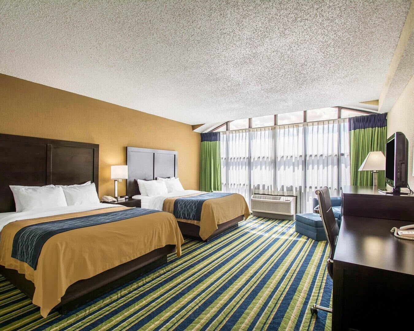 Une chambre d’hôtel avec deux lits, un bureau avec un ordinateur et une grande fenêtre avec des rideaux.