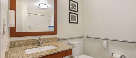 A bathroom with a granite countertop sink, a mirror, a toilet, and a hand sanitizer dispenser.