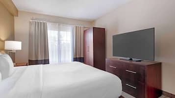 A hotel room with a large bed, a flat-screen TV on a wooden cabinet, a desk with a lamp, and a window with curtains.