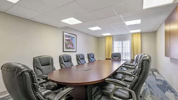 Un salón de conferencias con una larga mesa y varias sillas, un cuadro enmarcado en la pared y una ventana con cortinas amarillas.