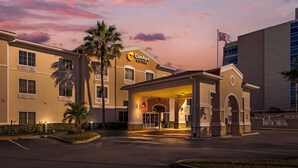 Entrada de hotel com área coberta, palmeiras e a bandeira dos Estados Unidos.