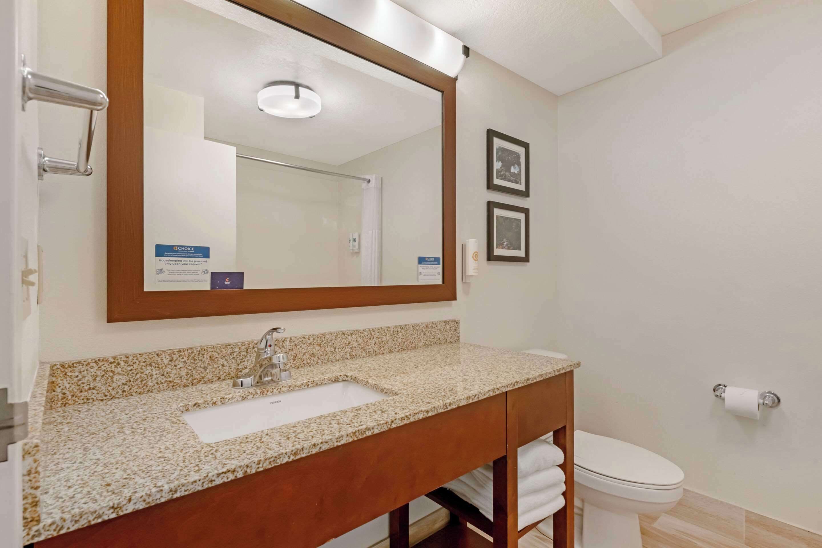 A bathroom with a granite countertop sink, a mirror, a toilet, and a towel rack.