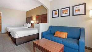 Quarto de hotel com duas camas, um sofá azul, uma mesa de madeira e quadros nas paredes.