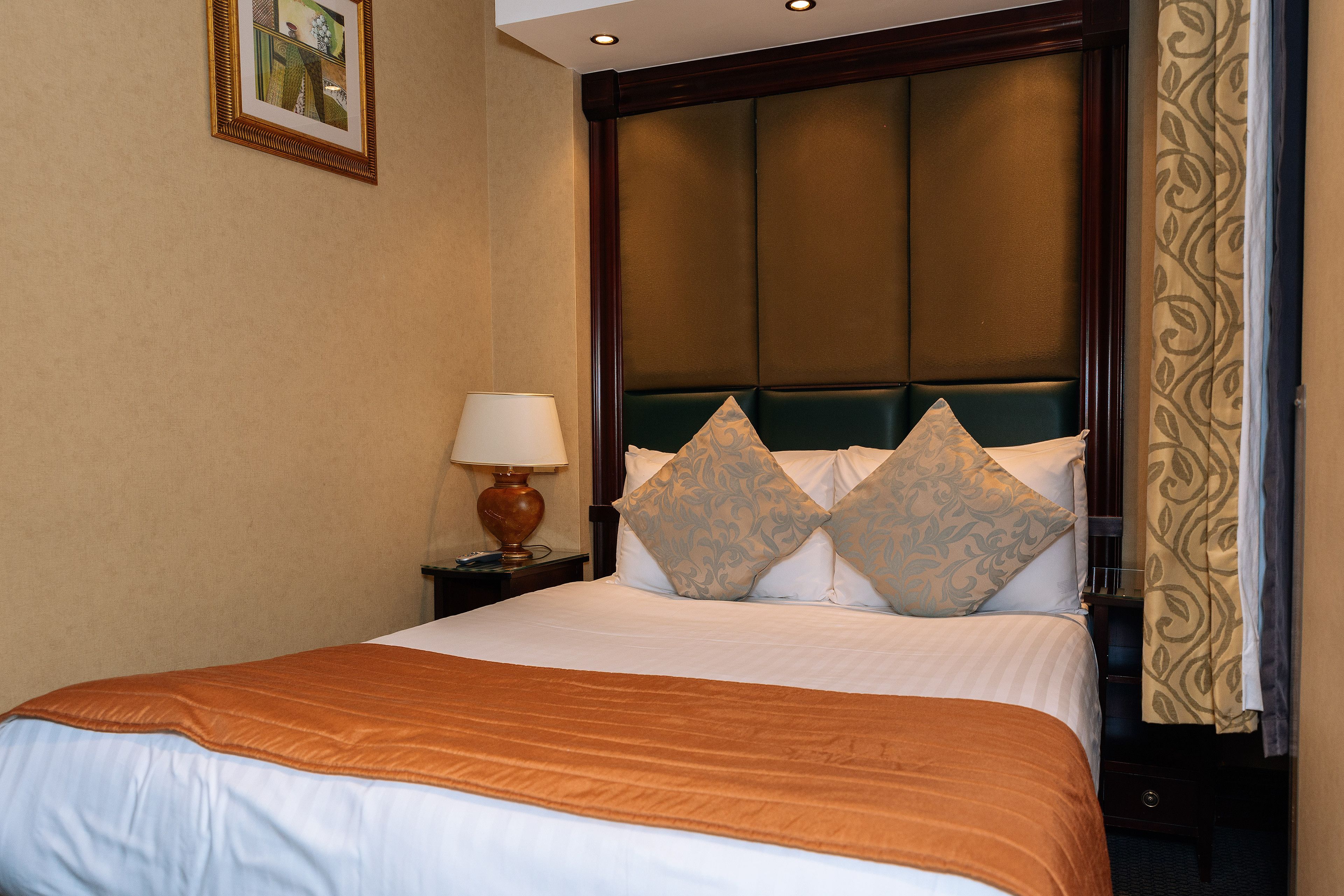 A hotel room with a large bed, a nightstand with a lamp, and a headboard with decorative pillows.