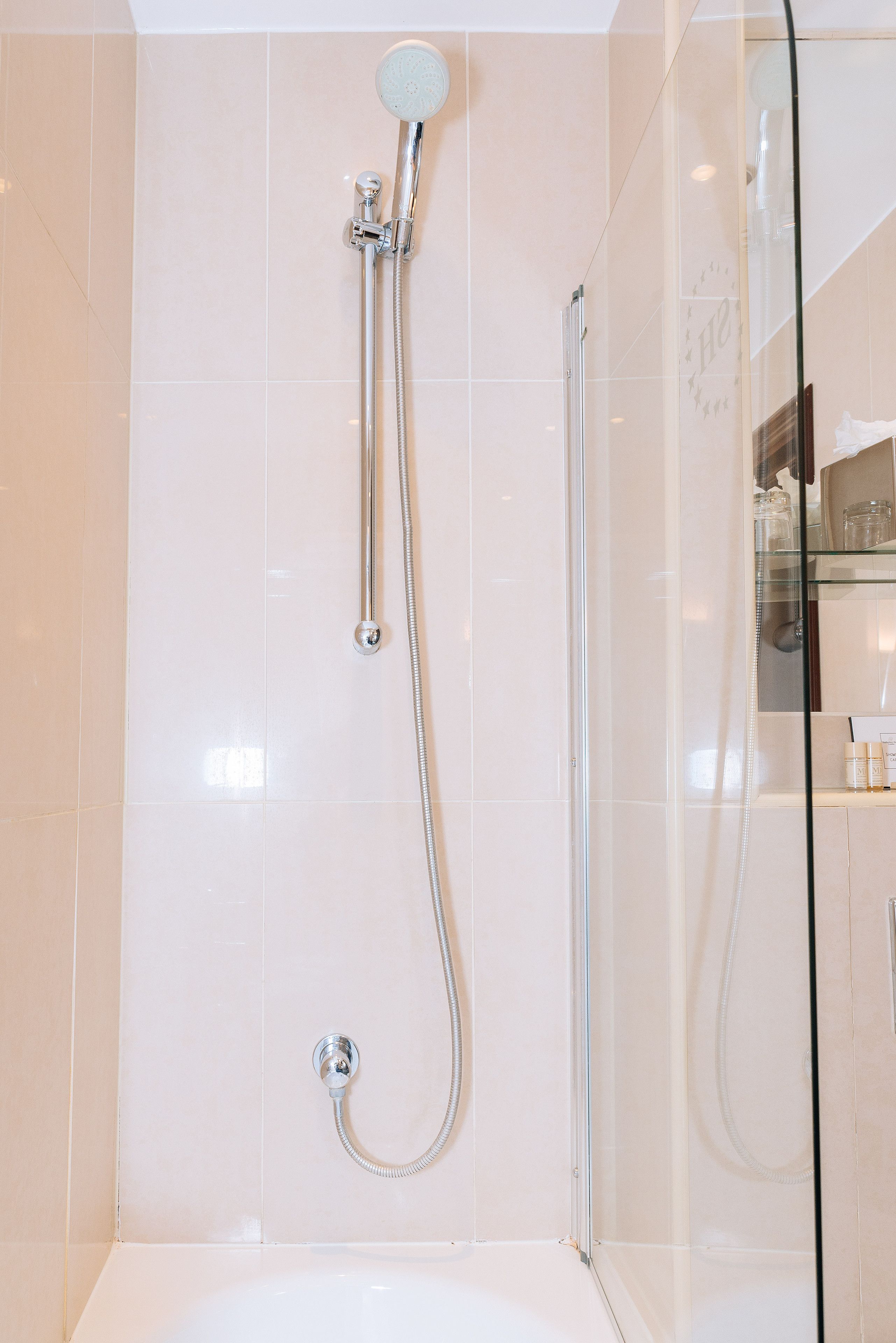 A modern bathroom with a glass-enclosed shower, a handheld showerhead, and a wall-mounted faucet.