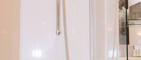 A modern bathroom with a glass-enclosed shower, a handheld showerhead, and a wall-mounted faucet.