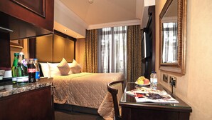 A hotel room with a bed, a desk with a chair, a mirror, and a window with curtains. - The Premier Notting Hill (London)