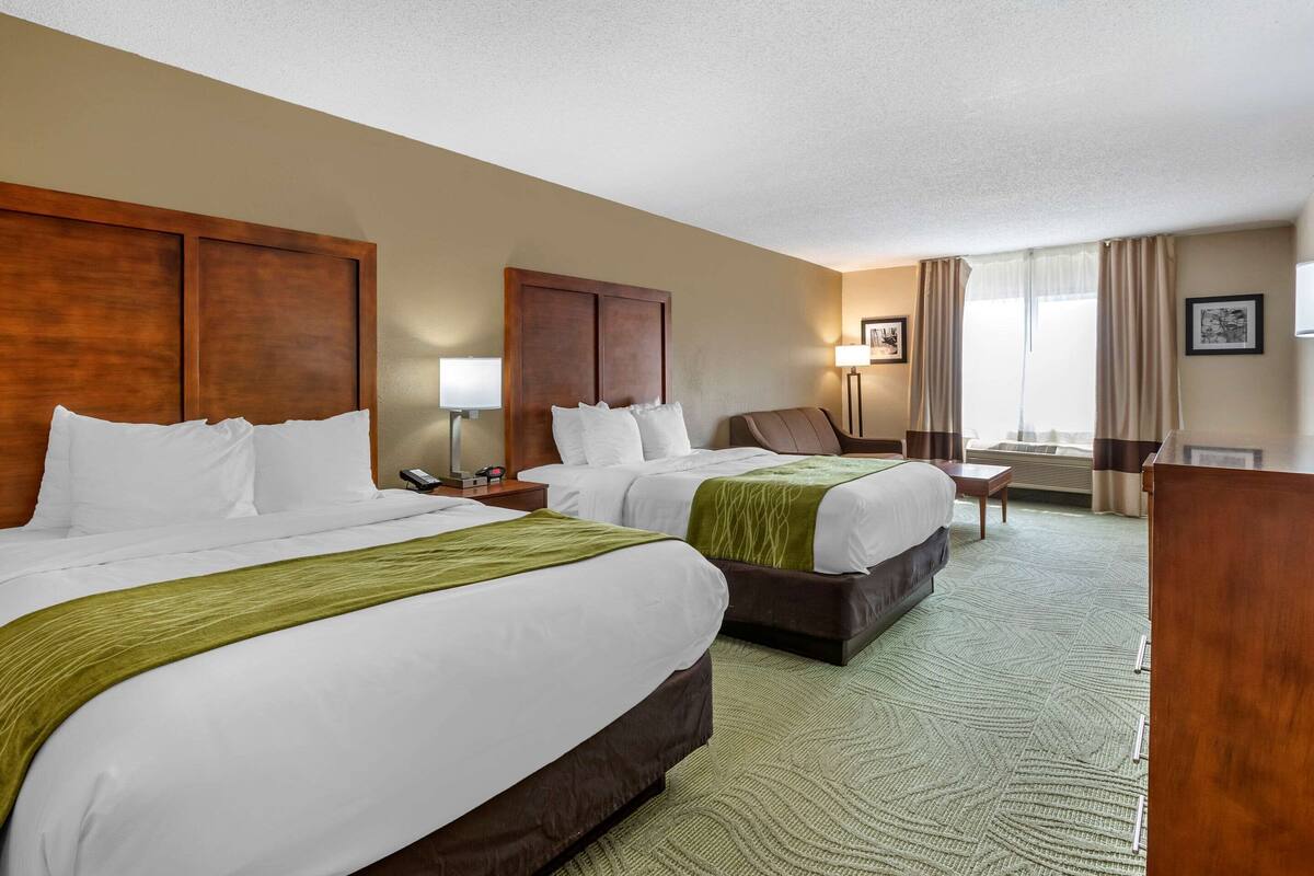 A hotel room with two beds, a desk, a chair, a lamp, and a window with curtains.