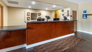 A reception area with a wooden counter, a reception desk, a digital kiosk, and a patterned rug. - Comfort Inn Muscatine near Hwy 61 (Muscatine)