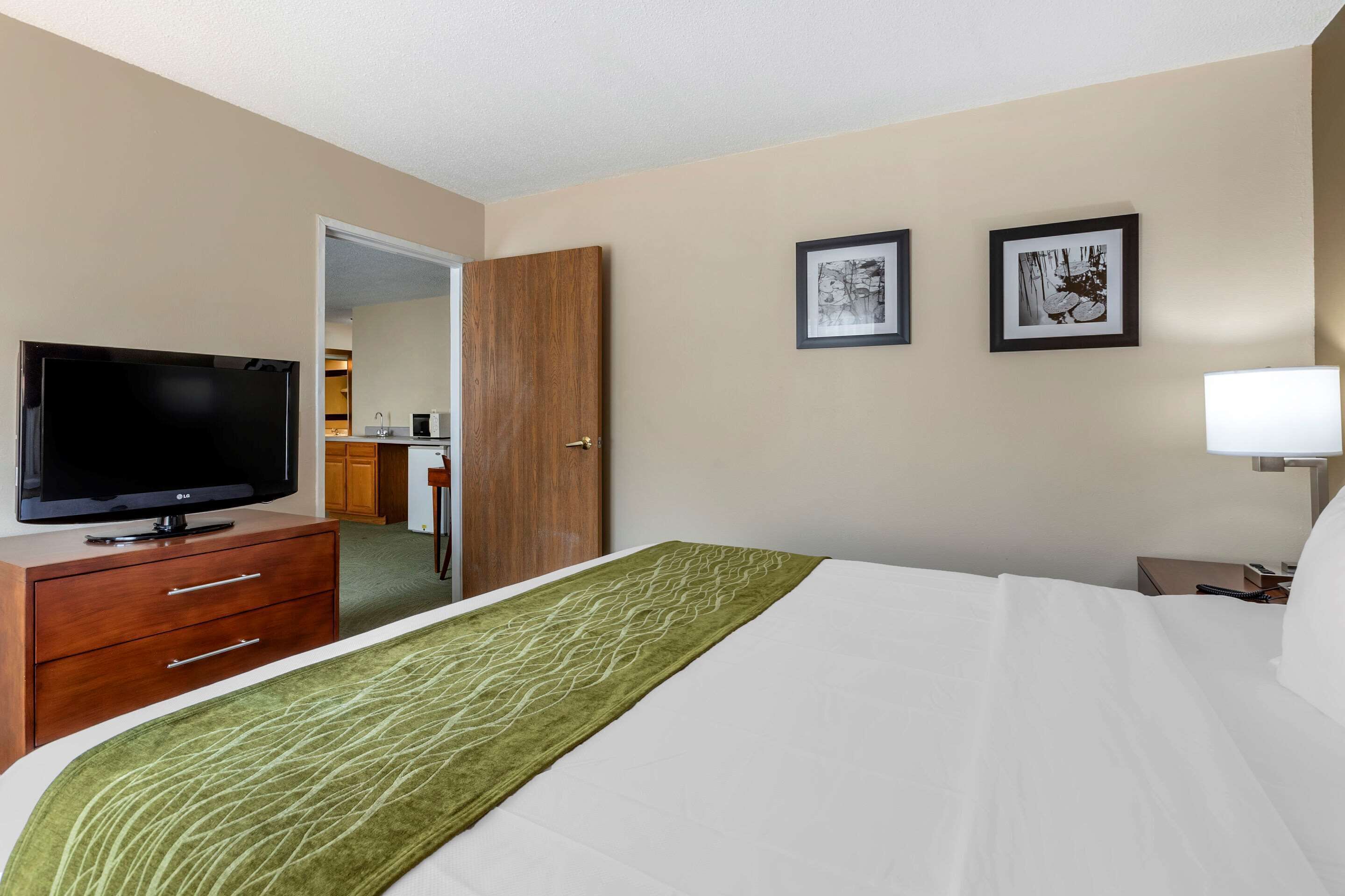 A hotel room with a bed, a TV, a desk, and a door leading to a bathroom.