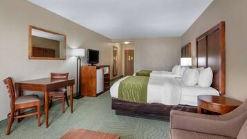 Quarto de hotel com cama, escrivaninha, cadeira, televisão e mesa pequena.