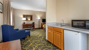 A compact hotel room with a kitchenette, a blue sofa, a desk with a chair, a small refrigerator, and a microwave. - Comfort Inn Muscatine near Hwy 61 (Muscatine)