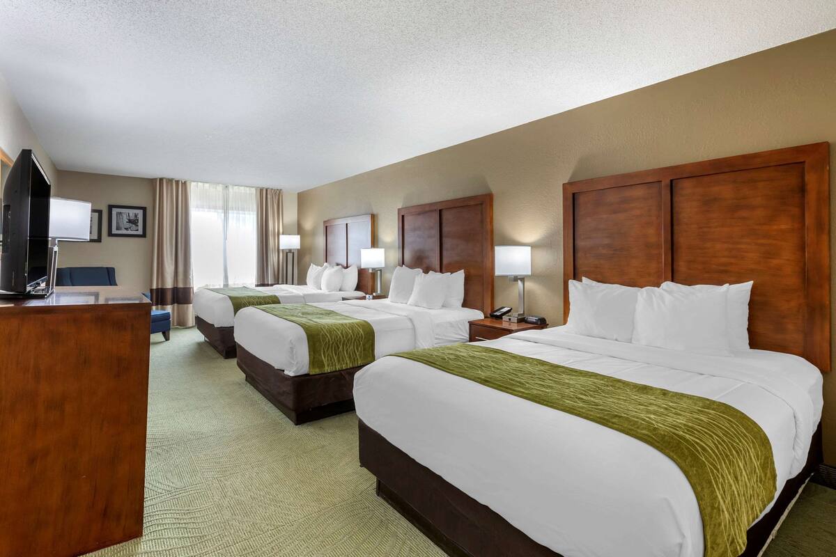 A hotel room with three beds, a desk, and a television.