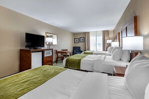 A hotel room with three beds, a TV, a desk with a computer, and a chair.