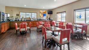 A restaurant with wooden flooring, red upholstered chairs, and a kitchen area with various appliances. - Comfort Inn Muscatine near Hwy 61 (Muscatine)