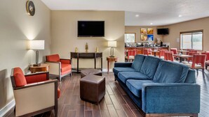 A hotel lobby with a sofa, chairs, a TV, a dining area, and a clock on the wall. - Comfort Inn Muscatine near Hwy 61 (Muscatine)