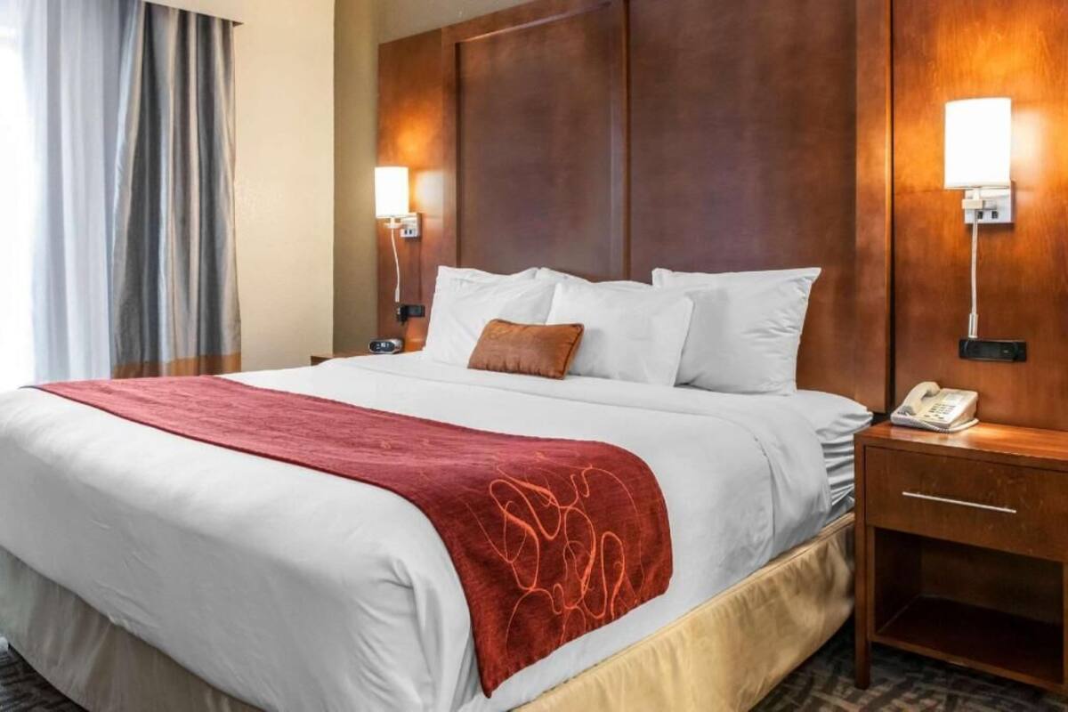 A hotel room with a large bed, a wooden headboard, two bedside lamps, a telephone, and a red throw blanket.