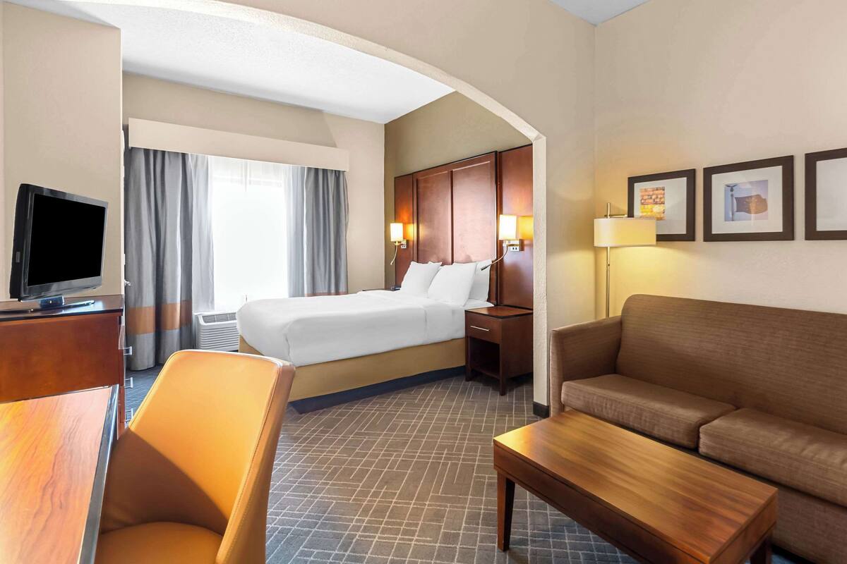 A hotel room with a bed, a desk, a chair, a sofa, and a television.