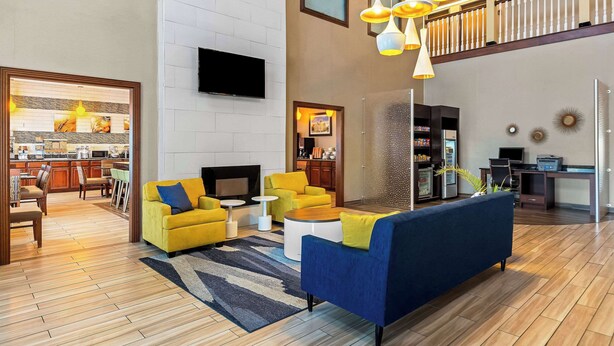 A spacious living area with a modern sofa, yellow armchairs, and a coffee table. A flat-screen TV is mounted on the wall, and there is a staircase leading to an upper level.