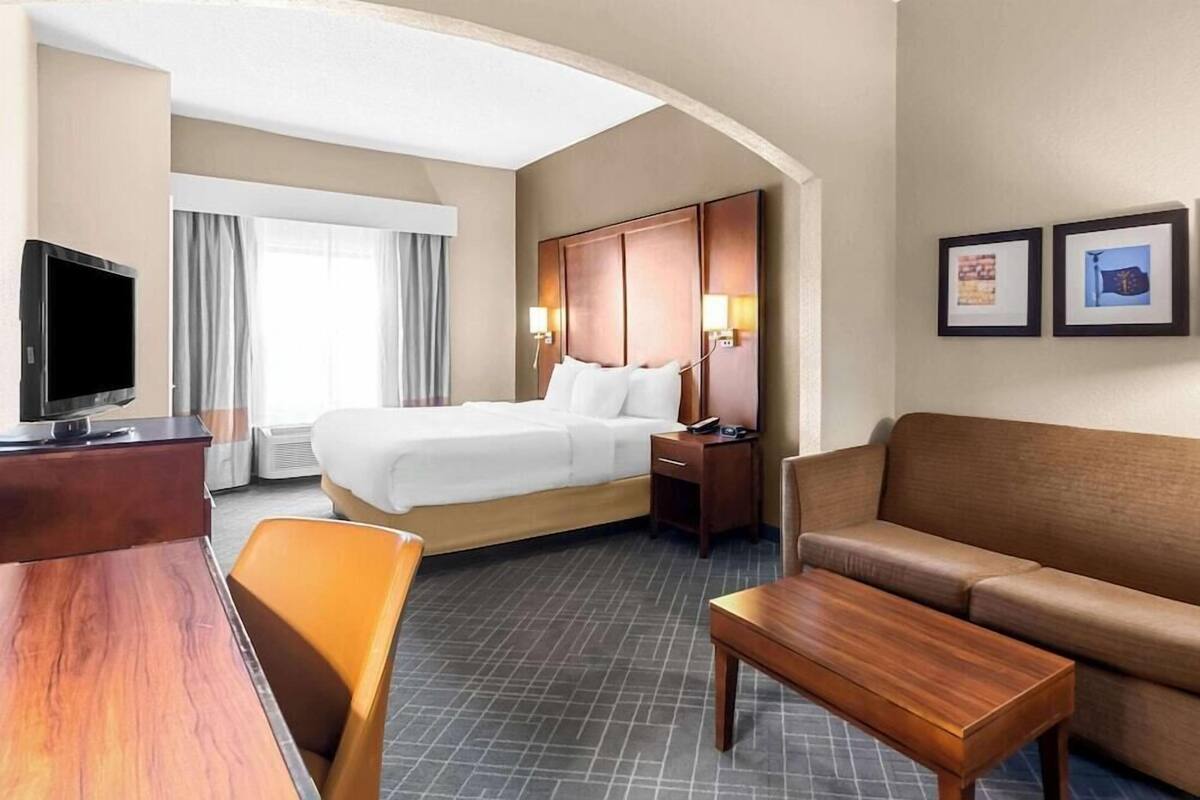 A hotel room with a bed, a TV, a desk, a sofa, and a coffee table.