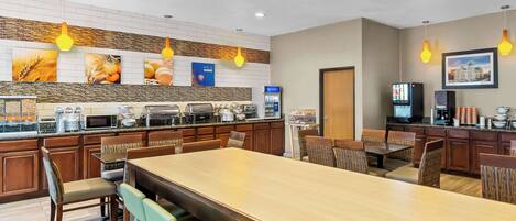 A modern kitchen with a long dining table, wooden chairs, and a variety of appliances.