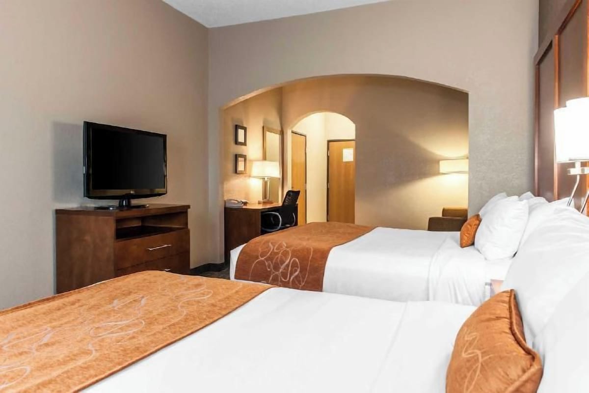 A hotel room with two beds, a TV, a desk, and a lamp.