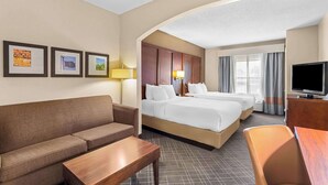 A hotel room with a sofa, two beds, a TV, and framed pictures on the wall.