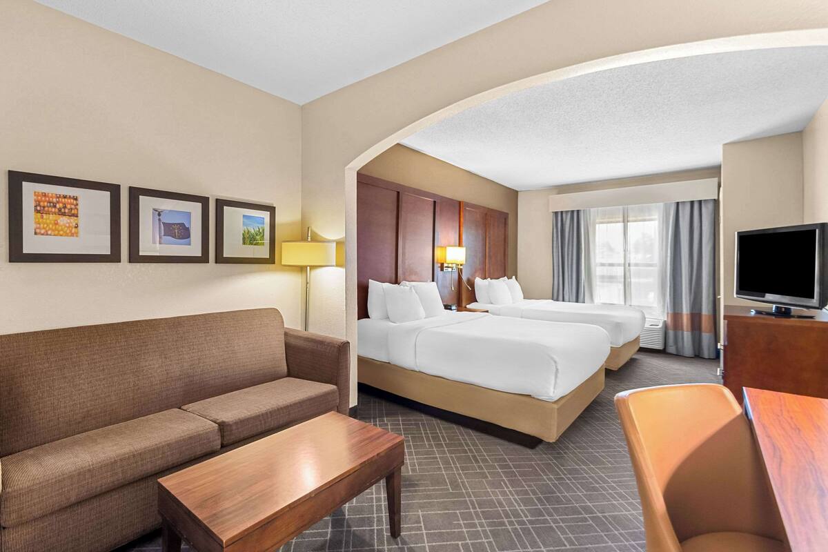 A hotel room with a sofa, two beds, a TV, and framed pictures on the wall.