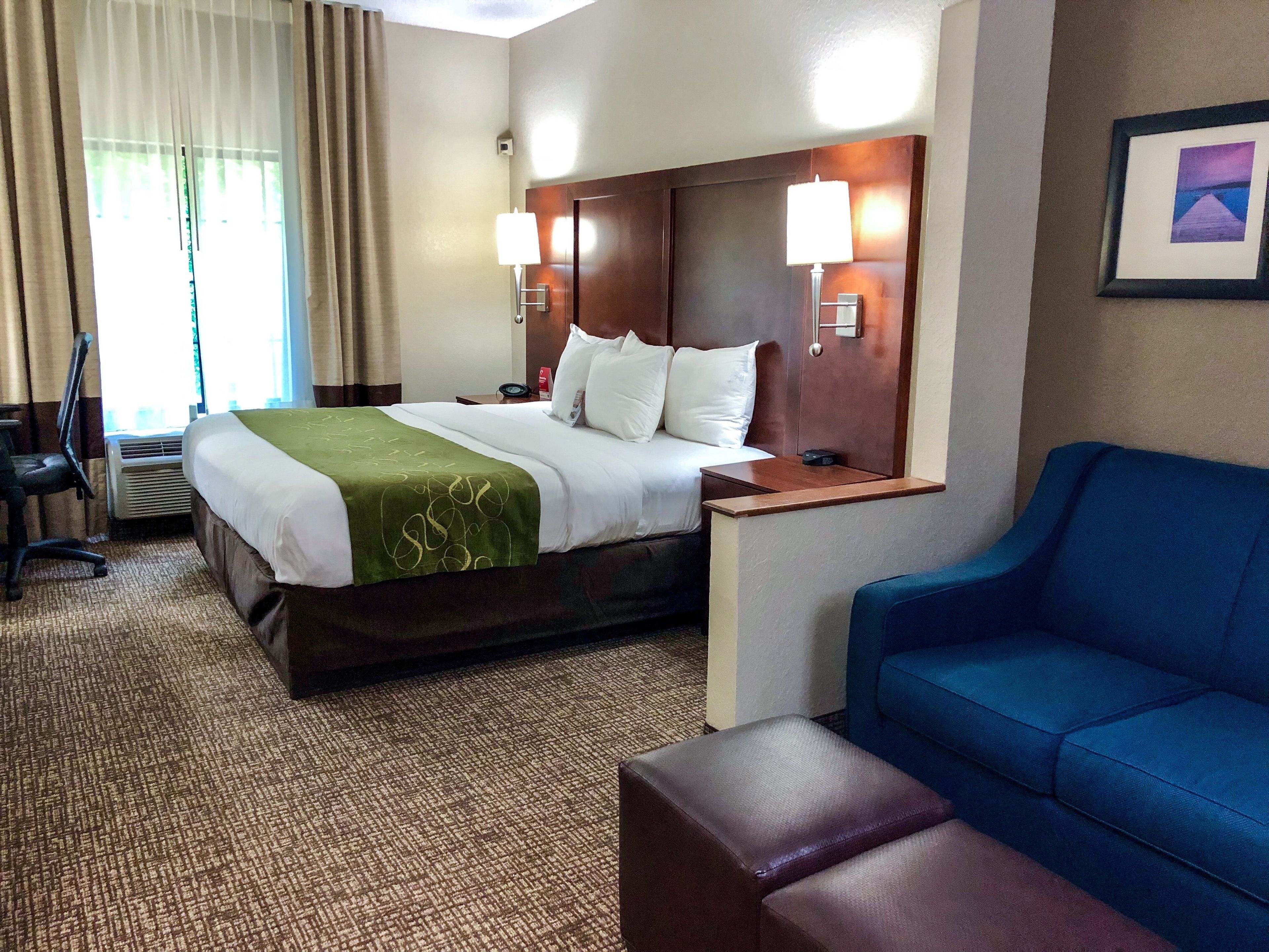 Ein Hotelzimmer mit Bett, blauem Sessel, Holz-Kopfteil, Nachttisch und Lampe.