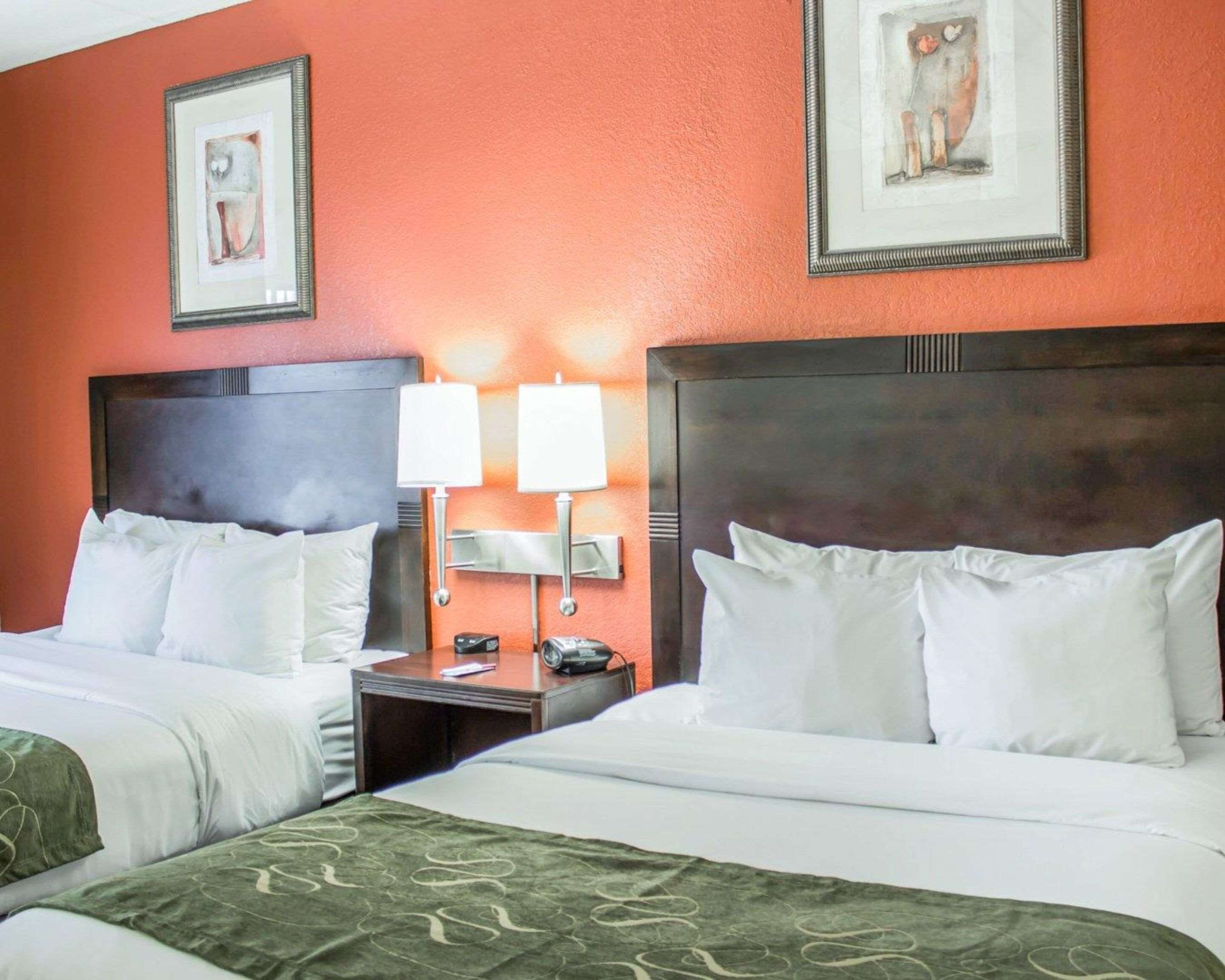A hotel room with two beds, a nightstand with lamps, and artwork on the walls.
