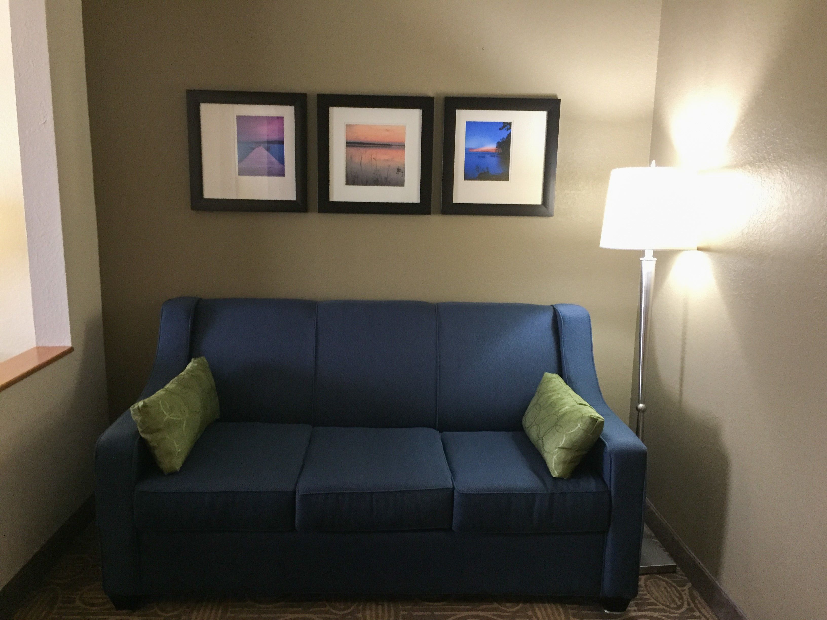 A blue sofa with two green pillows, a framed picture above it, and a floor lamp to the right.
