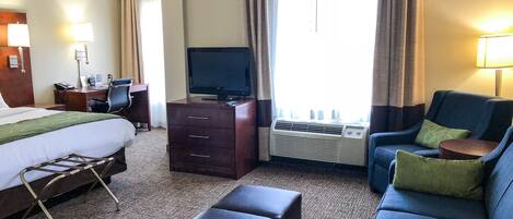 A hotel room with a bed, a desk, a television, a sofa, and an air conditioning unit.