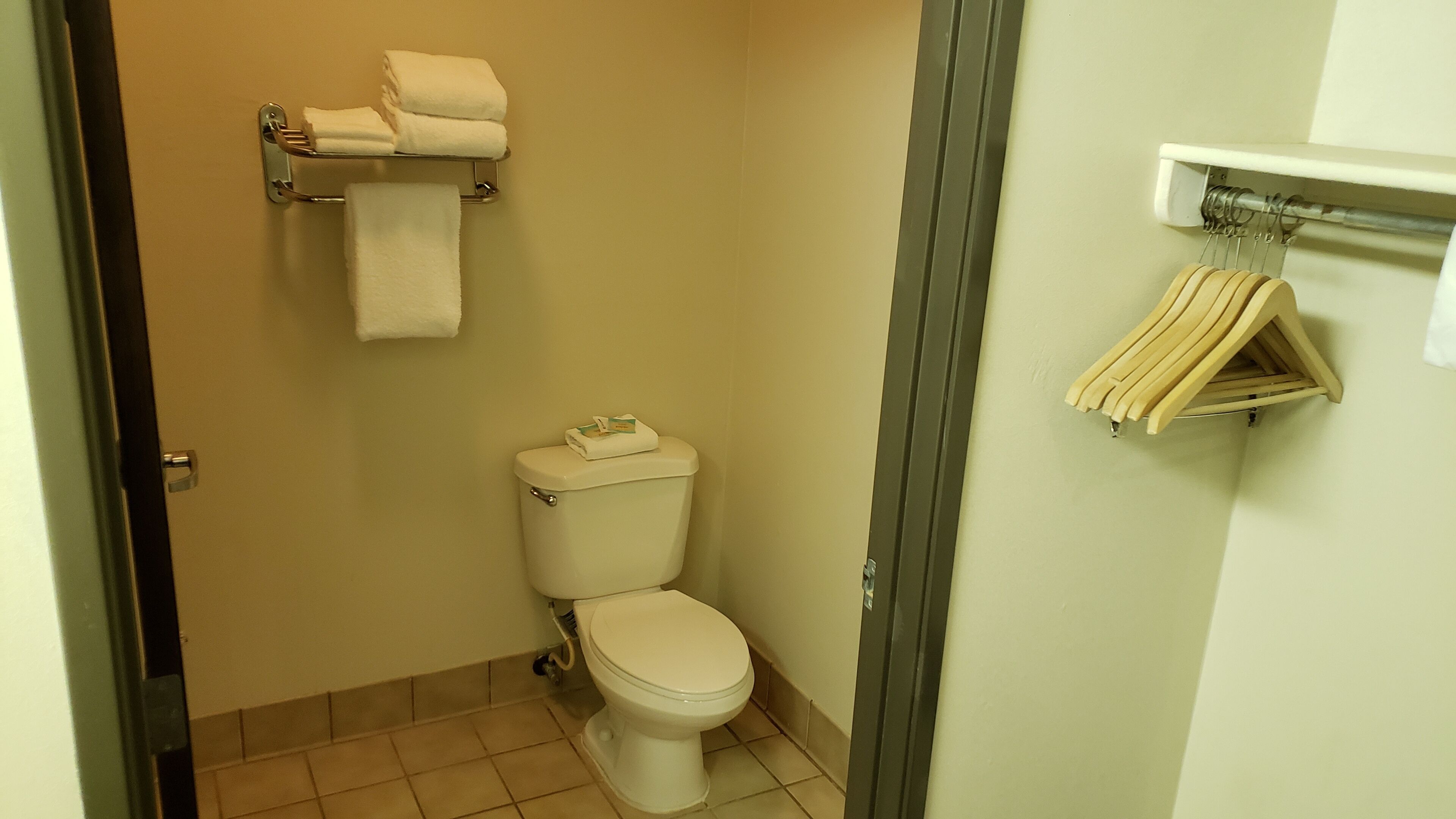 Casa de banho pequena com sanita, um porta-toalhas com toalhas dobradas e uma prateleira com toalhas penduradas.