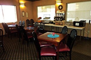 Un comedor con mesa de madera, sillas negras y un mostrador tipo buffet con comida y bebidas.