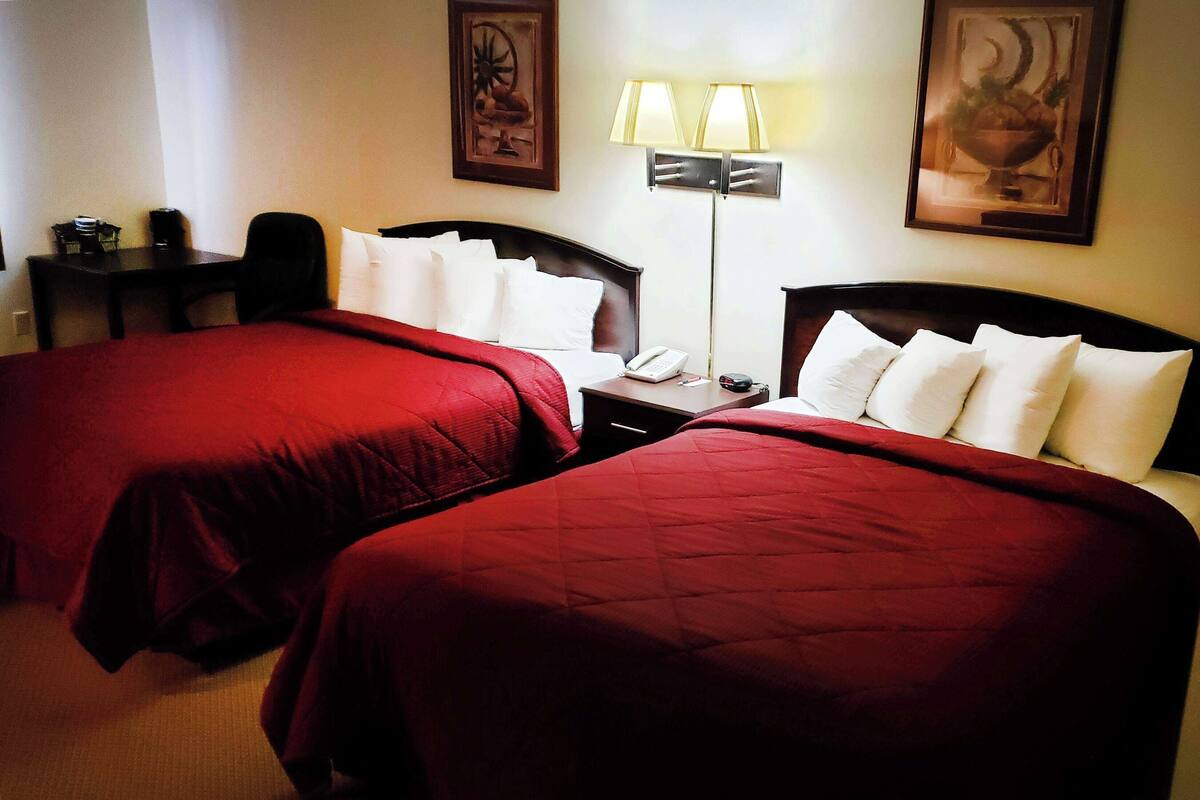 Une chambre d’hôtel avec deux lits, un bureau, une chaise, une lampe et un téléphone.