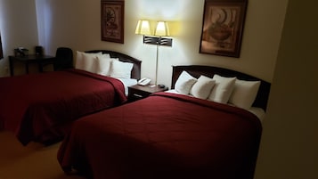 A hotel room with two beds, a desk, a lamp, and a phone.