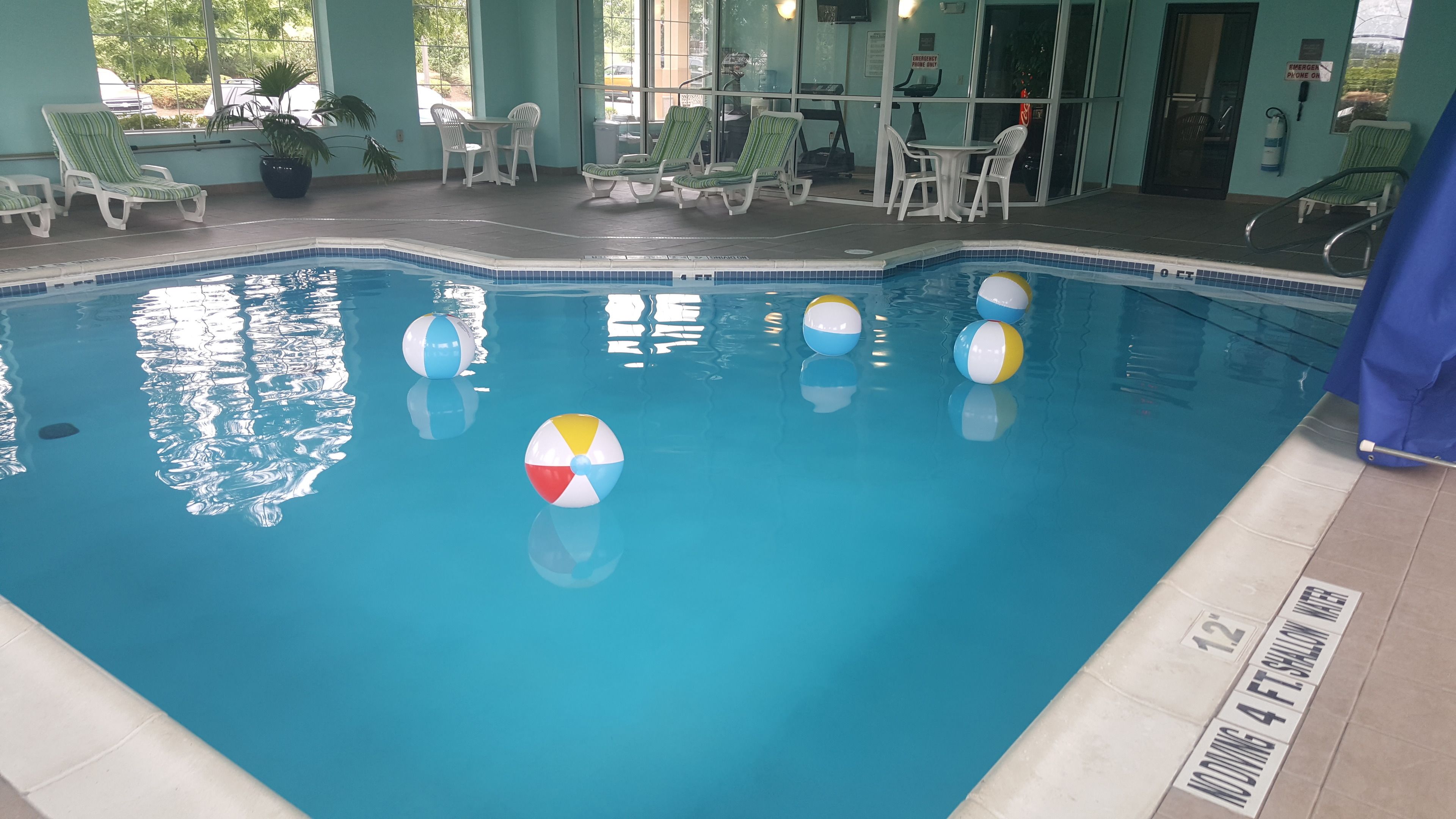 An indoor swimming pool with lounge chairs and tables, clear pool water, and a lifeguard station.