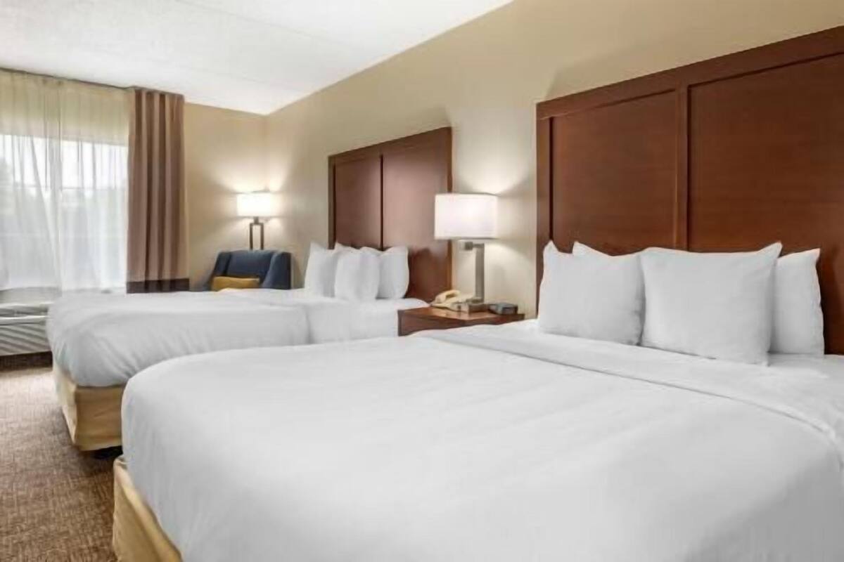 Une chambre d’hôtel avec deux lits, un bureau avec une lampe, une chaise et une fenêtre avec des rideaux.