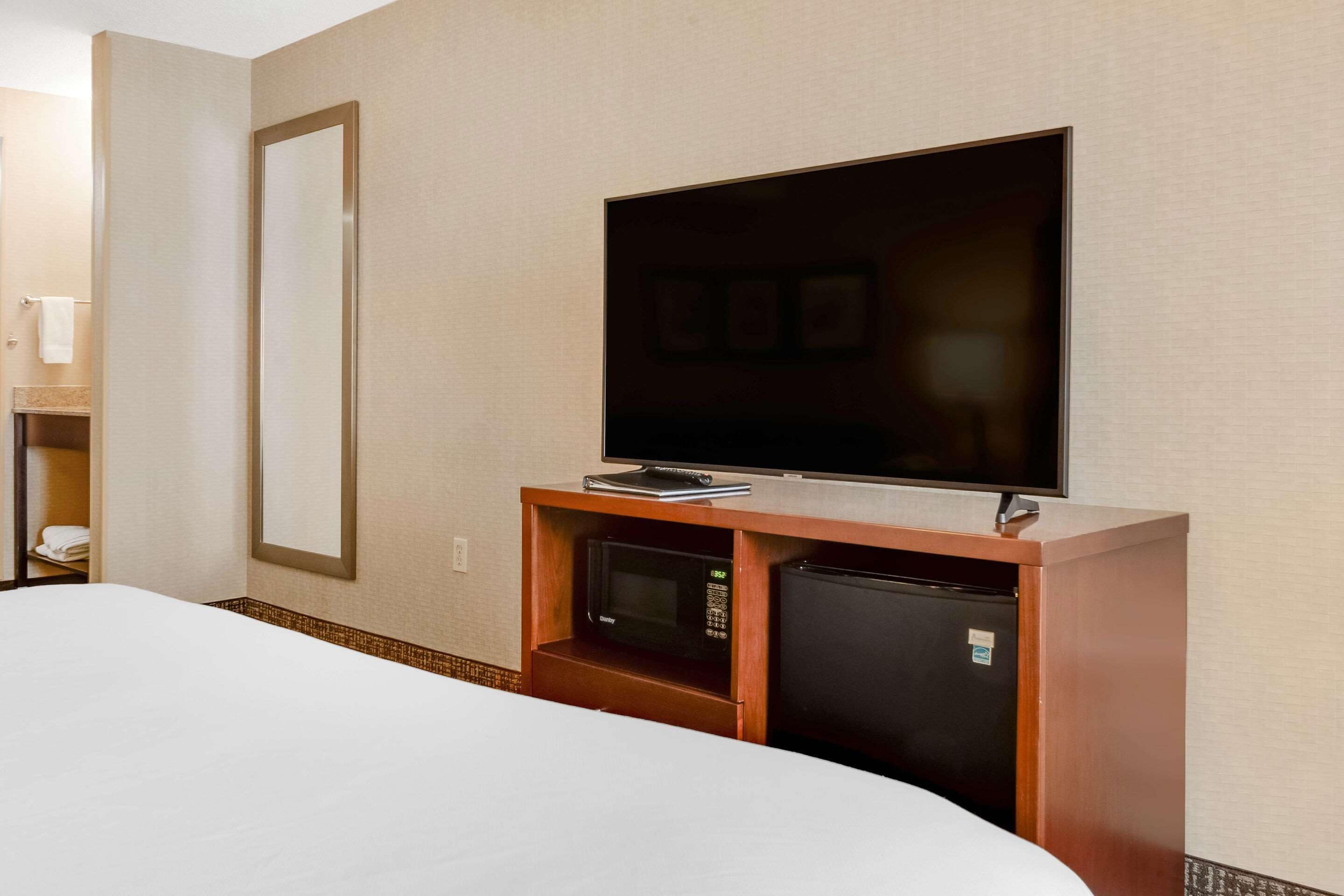 A hotel room with a bed, a television mounted on a wooden cabinet, a microwave, and a refrigerator.