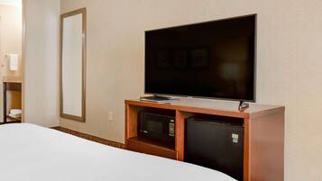 A hotel room with a bed, a television mounted on a wooden cabinet, a microwave, and a refrigerator.