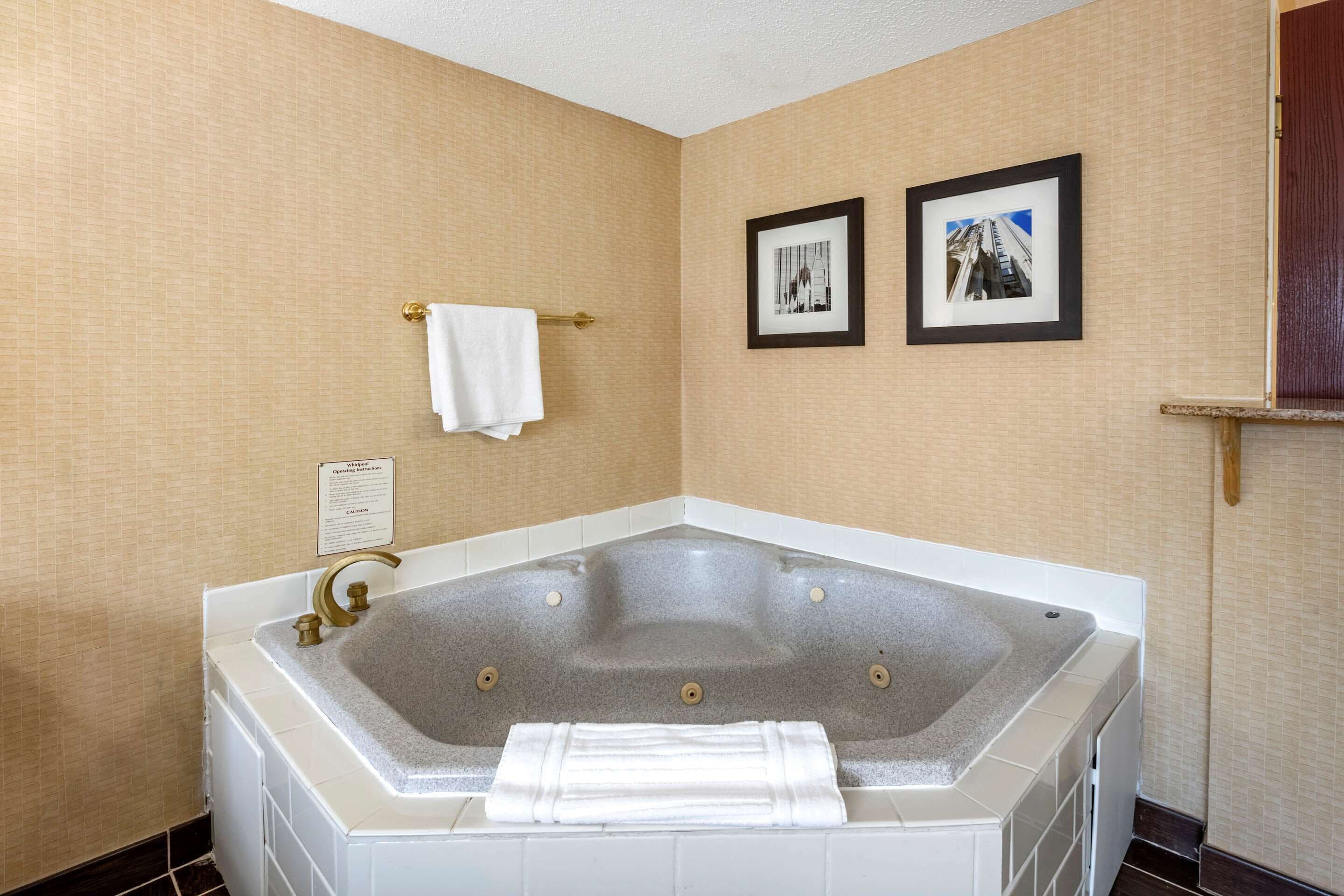 A bathroom with a large bathtub, a towel rack, and two framed pictures on the wall.