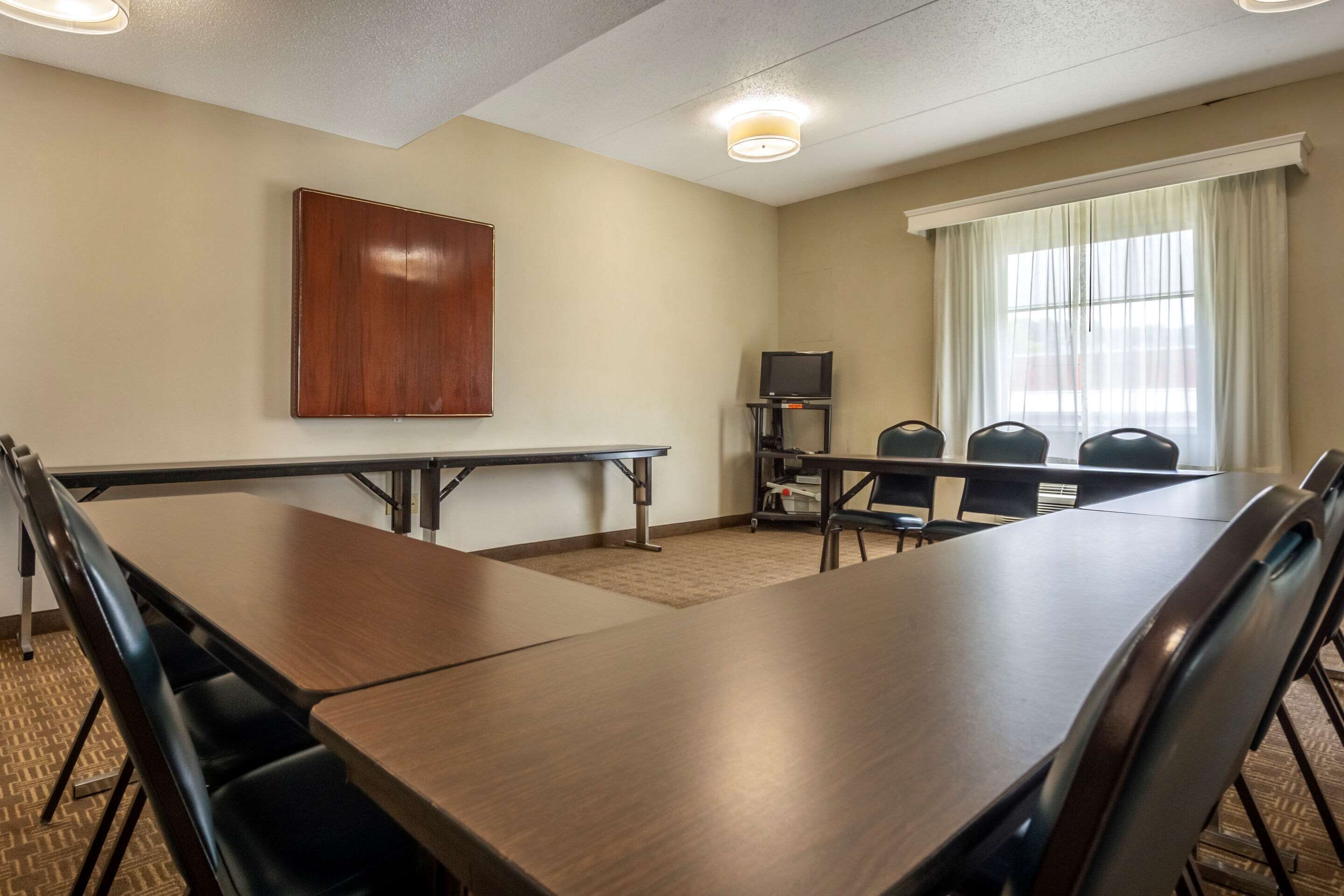 A conference room with a long table, chairs, a TV, and a window with curtains.